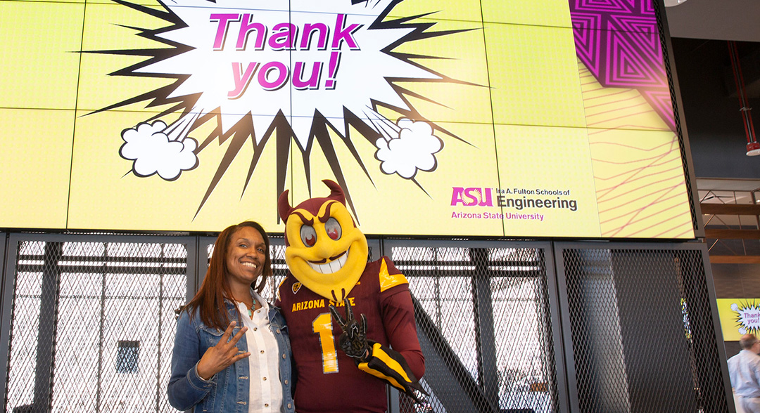 Woman poses with Sparky in front of a giant 'Thank you' banner.